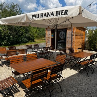 Ein gemütlicher Biergarten mit rustikalen Holzmöbeln und Sonnenschirmen bietet Platz für zahlreiche Gäste.