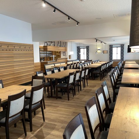 Ein stilvoll gestalteter Raum mit langen Holztischen und eleganten Stühlen, ideal für gesellige Zusammenkünfte oder Veranstaltungen.