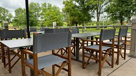 Eine einladende Terrasse mit Holzstühlen und Tischen, umgeben von Bäumen.