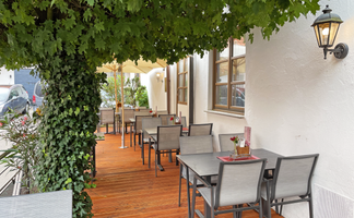 Schattige Restaurantterrasse mit modernen Tischen und Stühlen, umgeben von Pflanzen und einer einladenden Atmosphäre.