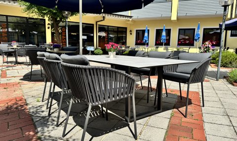 Ein sonniger Cafébereich mit eleganten Stühlen und einem Tisch, der auf eine entspannte Atmosphäre im Freien hinweist.