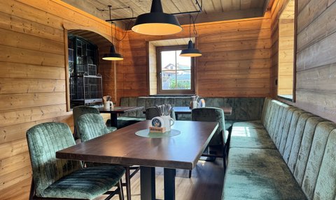Der Innenraum eines rustikalen Restaurants mit Holzdecke, eleganten Lampen und einer einladenden Sitzbank aus Samt.