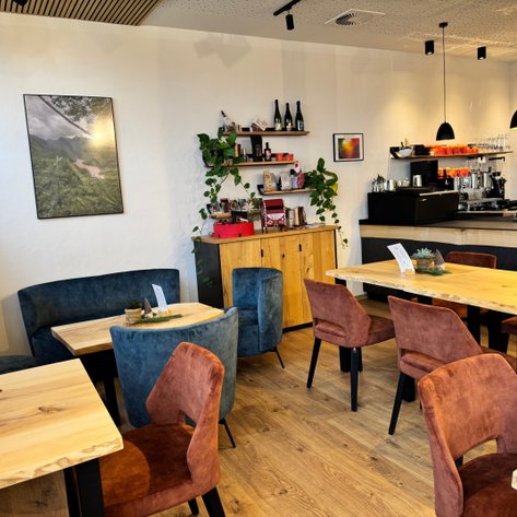 Ein einladendes Café mit holzfarbenen Tischen und bequemen Stühlen in Erdtönen, umgeben von grünen Pflanzen.