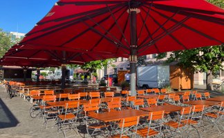 Weitläufige Freifläche mit Biergartentischen und -stühlen unter beschattenden Sonnenschirmen im Herzen von Ingolstadt.