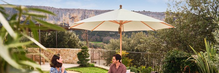 Zwei Personen sitzen unter einem beigen, aufgespannten Sonnenschirm von Glatz