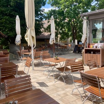 Sonnige Terrasse eines Restaurants, bestückt mit Tischen und Stühlen, bereit für Gäste, die das schöne Wetter genießen wollen.