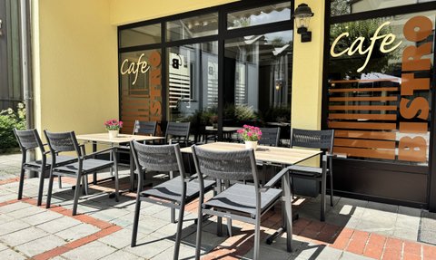 Ein sonniger Cafébereich mit eleganten Stühlen und einem Tisch, der auf eine entspannte Atmosphäre im Freien hinweist.