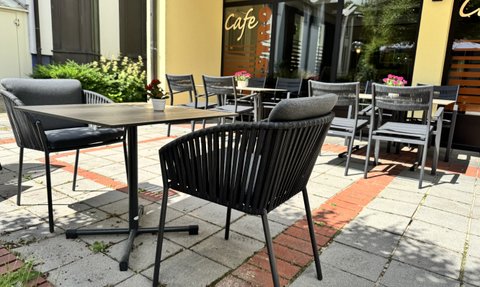 Ein sonniger Cafébereich mit eleganten Stühlen und einem Tisch, der auf eine entspannte Atmosphäre im Freien hinweist.