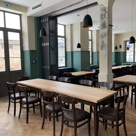 Helles, klassisches Restaurant mit Holzstühlen und großen Fenstern, das eine einladende Atmosphäre schafft.