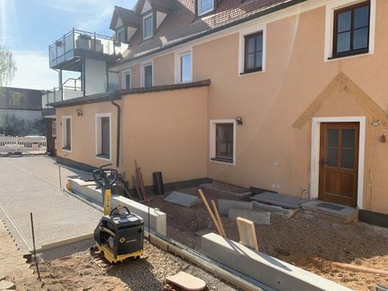 Der Eingangsbereich eines Hauses wird renoviert, mit Baustellenmaterialien und unvollendeten Arbeiten sichtbar im Vordergrund.