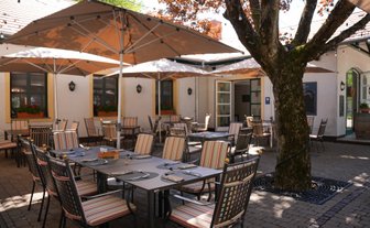 Gemütliche Terrasse mit eleganten Tischen und Stühlen, die auf einen sonnigen Tag in einem Restaurant hinweist.