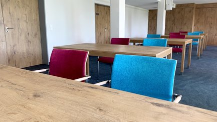 Ein moderner Besprechungsraum mit gut beleuchteten Tischen und bequemen Stühlen, der zur kreativen Zusammenarbeit einlädt.