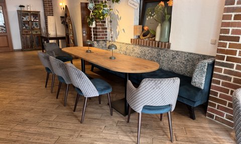 Der Innenraum zeigt eine gemütliche Sitzecke mit einer blauen Bank, einem großen Tisch und modernen Vollpolsterstühlen.