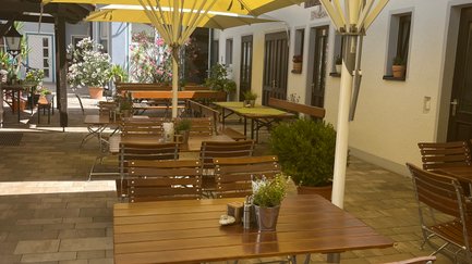 Sonnige Terrasse eines Restaurants, bestückt mit Tischen und Stühlen, bereit für Gäste, die das schöne Wetter genießen wollen.