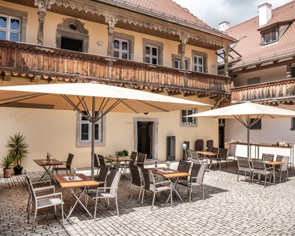 Ein gemütlicher Innenhof mit Tischen und Stühlen unter großen Sonnenschirmen, umgeben von historischen Gebäuden.