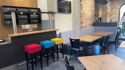 Modernes Café-Interieur mit bunten Barhockern in Rot, Blau und Gelb, einer Holztheke und eleganten Sitzbereichen.