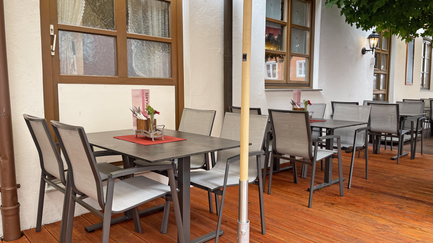 Schattige Restaurantterrasse mit modernen Tischen und Stühlen, umgeben von Pflanzen und einer einladenden Atmosphäre.
