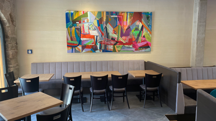Helle, komfortable Sitzbereiche in einem Café, geschmückt mit einer kreativen Wandmalerei, die den Raum lebendig erscheinen lässt.