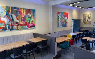 Holztische und gepolsterte Bänke verleihen dem Café eine entspannte Atmosphäre, geschmückt mit ausdrucksvoller Kunst.