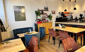 Ein einladendes Café mit holzfarbenen Tischen und bequemen Stühlen in Erdtönen, umgeben von grünen Pflanzen.