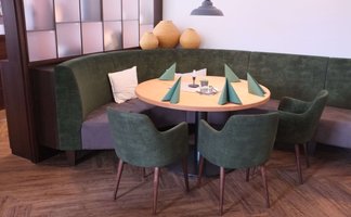 Die grüne Vollpolsterbank mit bunten Kissen und die hölzernen Tische sind perfekt für gesellige Abende in diesem modernen Restaurant.