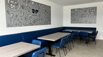 Die Einrichtung umfasst elegante blaue Stühle und Tische aus hellem Holz, ideal für geselliges Beisammensein.