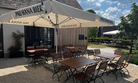 Ein gemütlicher Biergarten mit rustikalen Holzmöbeln und Sonnenschirmen bietet Platz für zahlreiche Gäste.
