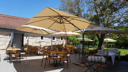 Die Terrasse eines Restaurants ist mit rustikalen Tischen und Stühlen gestaltet, umgeben von blühenden Pflanzen und historischer Architektur.