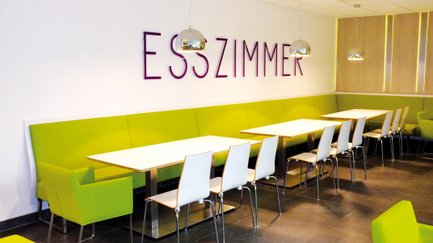 Ansicht eines Sitzbereichs mit einem weißen Tisch und grüngepolsterten Barhockern