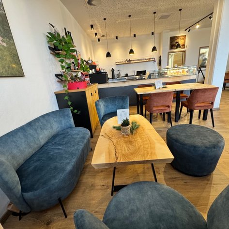 Der Innenraum eines einladenden Cafés mit stilvollen blauen Sitzgelegenheiten, einer rustikalen Holztisch und dekorativen Pflanzen.