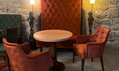 Ein eleganter Raum mit einem runden Tisch und zwei orangenen Sesseln vor einer gepolsterten Wand, vermischt mit rustikalen Steinen.