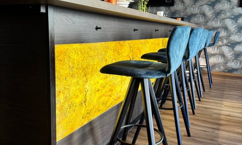 Die Bar ist mit einer leuchtenden Thekenverkleidung und stilvollen, blauen Hockern ausgestattet, die eine gemütliche Stimmung schaffen.
