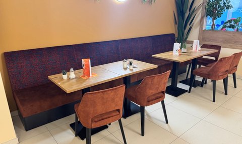 Die gemütliche Café-Ecke zeigt Holztische mit bequemen, samtigen Stühlen, eine entspannte Atmosphäre lädt zum Verweilen ein.