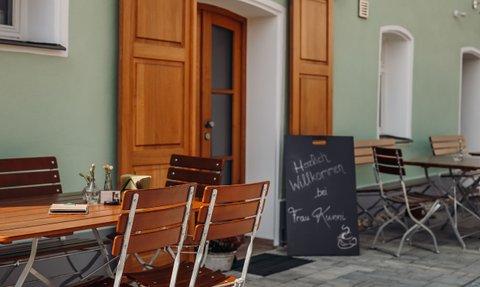 Tische und Stühle im Freien, ideal für Kaffeepausen, mit einem Willkommensschild für Gäste von Frau Kunni.