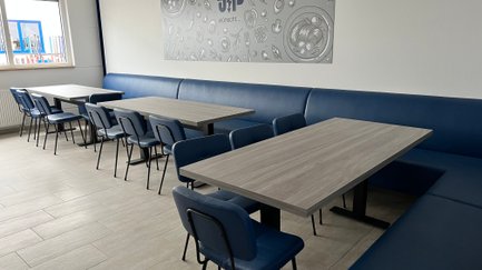 Die Einrichtung umfasst elegante blaue Stühle und Tische aus hellem Holz, ideal für geselliges Beisammensein.