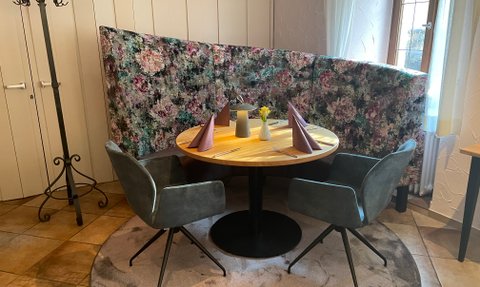 Die gepolsterte Rundbank mit buntem Blumenmuster ergänzt den runden Holztisch im gemütlichen Essbereich.