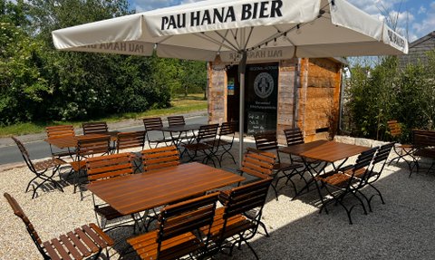 Ein gemütlicher Biergarten mit rustikalen Holzmöbeln und Sonnenschirmen bietet Platz für zahlreiche Gäste.