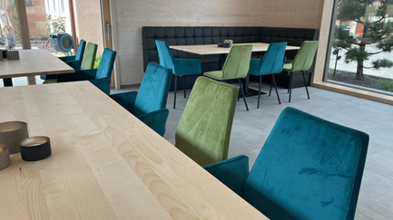 Ein heller, einladender Innenraum mit modernen Holztischen und Stühlen in lebendigen Farben, perfekt für gesellige Zusammenkünfte.