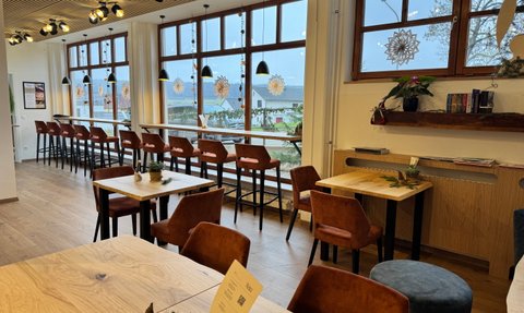 Eine stilvolle Café-Umgebung mit Holzstühlen und Tischen, großen Fenstern und modernen Dekorationselementen.