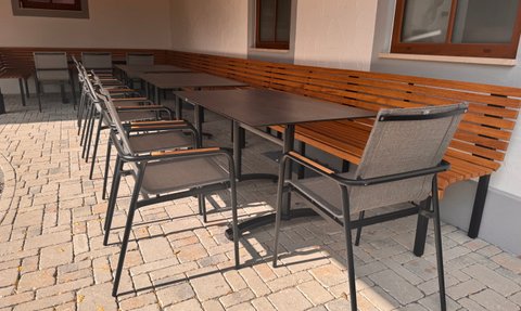 In einem gemütlichen Gartenbereich sind eine Holzbank und mehrere Stühle um einen großen Tisch angeordnet, bereit für Gäste.