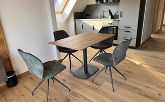 Elegante Stühle aus grauem Stoff um einen modernen Holztisch gruppiert, vor einer modernen Küchenzeile mit dunklen Akzenten.