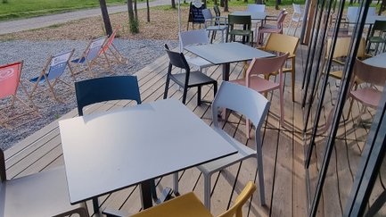 Auf der Terrasse des Cafés warten bunte Stühle und Tische auf Gäste, die die entspannte Atmosphäre im Freien genießen möchten.