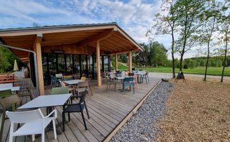 Auf der Terrasse des Cafés warten bunte Stühle und Tische auf Gäste, die die entspannte Atmosphäre im Freien genießen möchten.