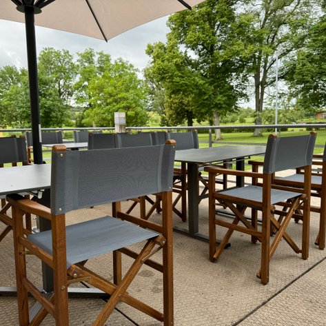 Eine einladende Terrasse mit Holzstühlen und Tischen, umgeben von Bäumen.