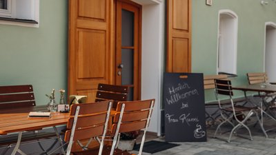 Tische und Stühle im Freien, ideal für Kaffeepausen, mit einem Willkommensschild für Gäste von Frau Kunni.