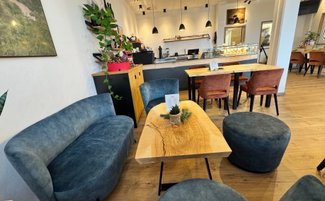 Der Innenraum eines einladenden Cafés mit stilvollen blauen Sitzgelegenheiten, einer rustikalen Holztisch und dekorativen Pflanzen.
