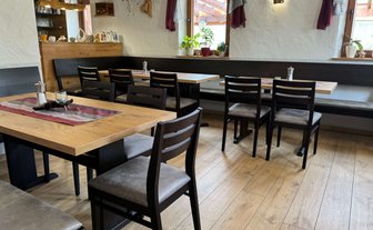 Der Innenraum eines gemütlichen Restaurants zeigt Holztische, Stühle und eine gemütliche Sitzbank.