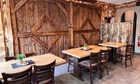 Einladende Tische mit Stühlen in einem gemütlichen Restaurant, umgeben von rustikalen Holzwänden und sanfter Beleuchtung.
