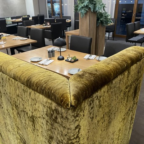 Der gepolsterte, goldene Teil des Sitzbereichs bietet Komfort und Auffälligkeit, während die Tische im Hintergrund schön gedeckt sind.