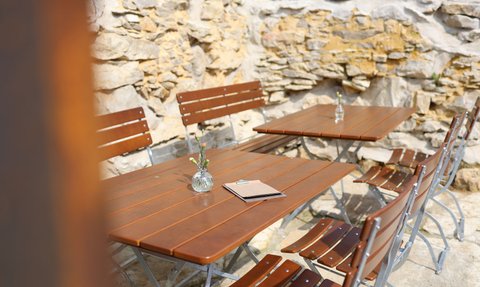 Mehrere Biergartentische und -stühle, umgeben von einer steinernen Wand, die eine einladende Atmosphäre schaffen.